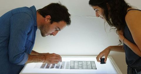 Photographers examining film strips with magnifying glass