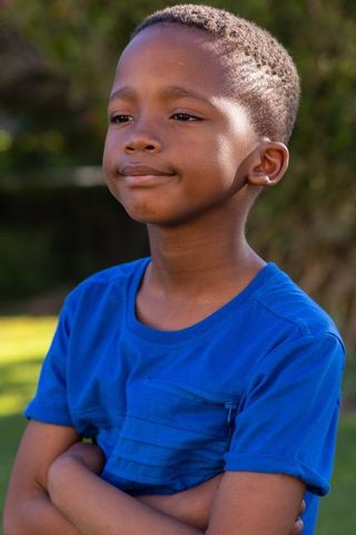 Confident african american boy standing arms crossed wearing royal blue tee in sunlit park