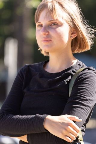 Young woman in 20s standing with arms crossed looking up in sunlit urban park