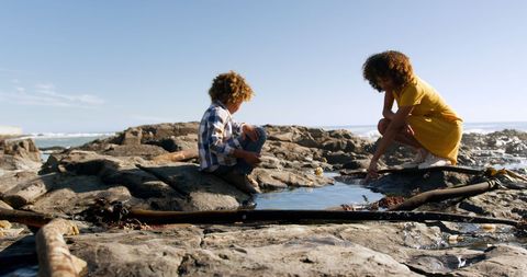 Mother and son exploring tide pools on rocky sunny beach