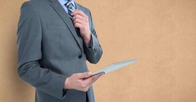 Midsection of businessman holding tablet PC over beige background - Download Free Stock Photos Pikwizard.com