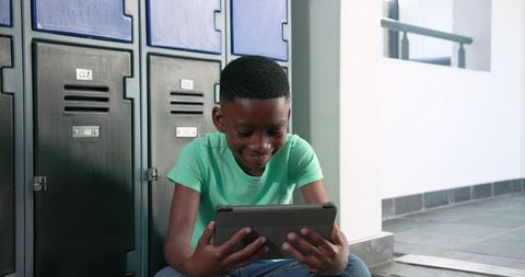 African-american teen using tablet while sitting beside school lockers, digital learning