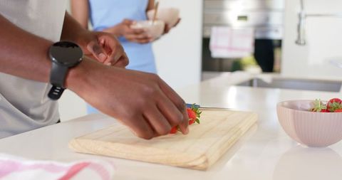 African american couple preparing strawberries on cutting board in bright modern kitchen