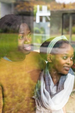 Two african american women looking out window together warm cozy autumn backyard reflection