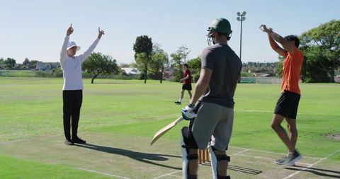 Asian indian umpire signalling six during cricket match with batsman and celebrating fielder