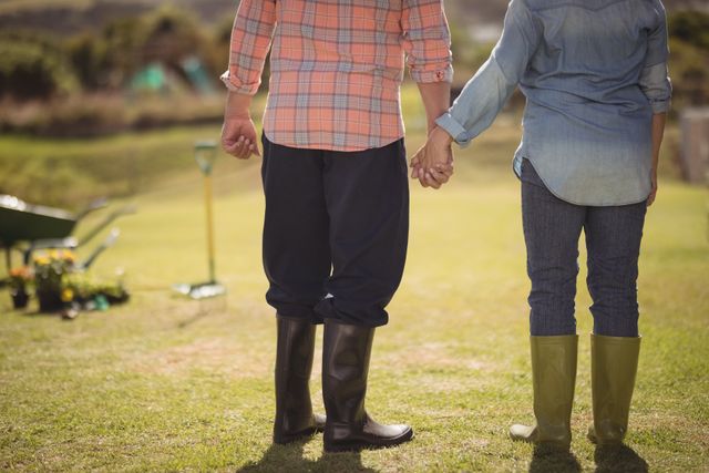 Lower section of senior couple holding hands and standing in their lawn on a sunny day