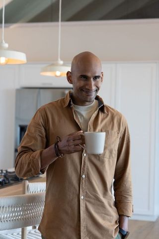 Asian man standing in modern minimal kitchen holding white mug smiling in cozy morning