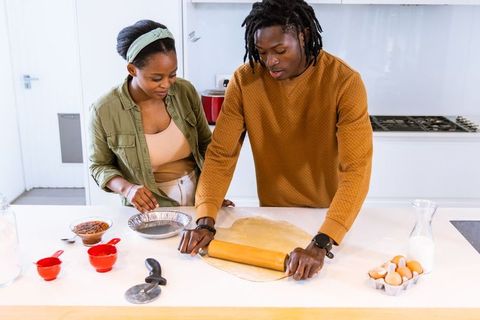 African american couple rolling dough together in bright modern kitchen for homemade pie