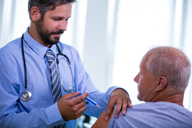 Male doctor administering an injection to a senior patient in a hospital setting. This image can be used for healthcare, medical treatment, vaccination campaigns, senior care, and hospital-related content. It highlights professional medical care and the importance of vaccinations and treatments for elderly patients.