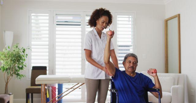 Biracial female physiotherapist helping senior man exercise using dumbbells. senior healthcare physiotherapy home visit.