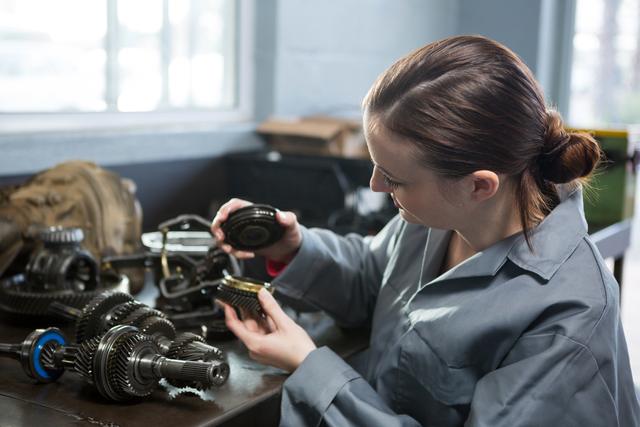 Attentive female mechanic holding spare parts of car at repair garage