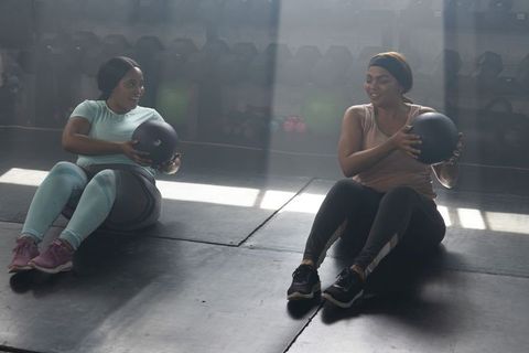 African american women performing medicine ball core workout in sunlit gym studio