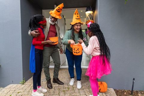 African american family celebrating halloween wearing pumpkin hats and sharing candy