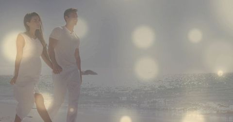 Walking Couple Holding Hands on Sunlit Shoreline in White Outfits with Bokeh Flares