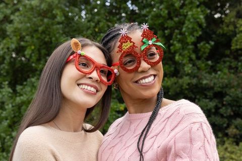 Smiling multicultural friends wearing festive red glitter glasses and cozy knit sweaters