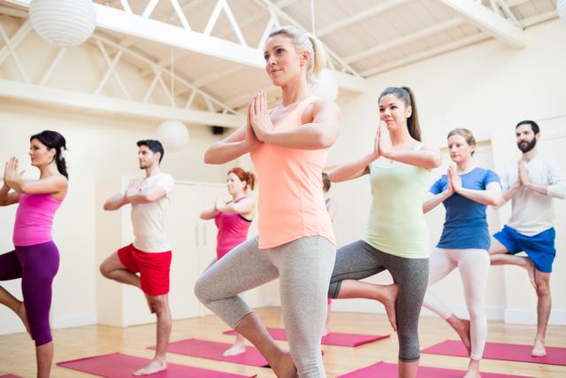 Group of people performing tree-pose yoga exercise in the fitness studio