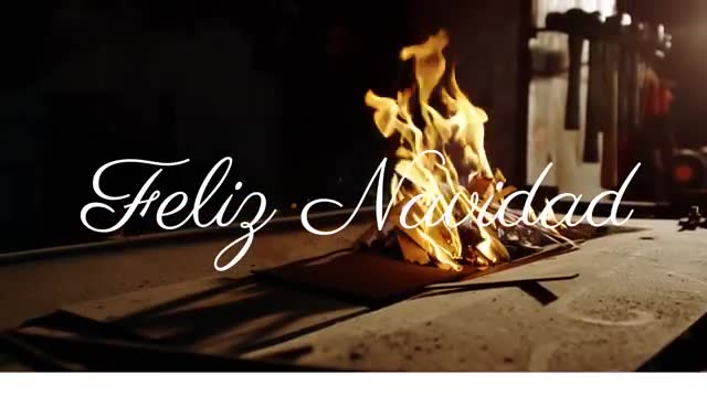 This artwork features the luminous 'Feliz Navidad' text hovering above burning papers, all illuminated by an open flame. The scene is enhanced by a dimly lit, moody atmosphere, embodying warmth and tradition often associated with the Christmas season. Perfect for use in festive cards, holiday invitations, or online promotional materials seeking to evoke traditional holiday sentiment and cozy interior scenes.