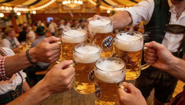Six beer steins clinking at bavarian festival tent with splashing foam and lively crowd