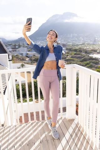 Smiling woman taking selfie on sunny deck with coffee and mountain view