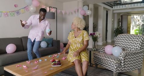 Expectant Black couple celebrating baby shower at home with pastel balloons and cupcakes