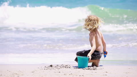 Blonde Child Playing at Beach with Shovel and Bucket Enjoys Sand and Waves