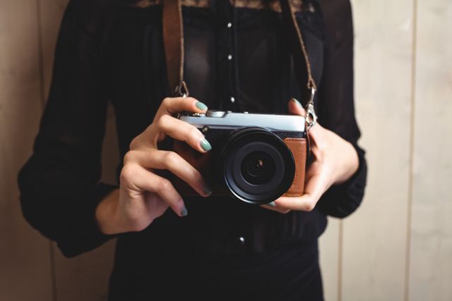 Mid-section of woman standing with camera against texture background