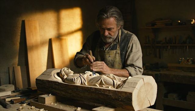 Senior woodcarver carving detailed wooden relief within log, rustic workshop artisan craft