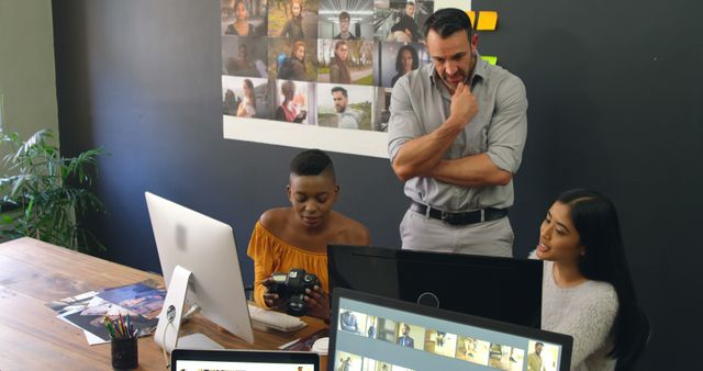 Diverse team reviews photos in an office setting. They collaborate on a creative project, analyzing images for selection.