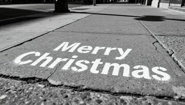 Stenciled merry christmas lettering showing on urban sidewalk black and white low angle