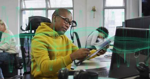Focused professional writing notes at coworking desk with tablet and monitor