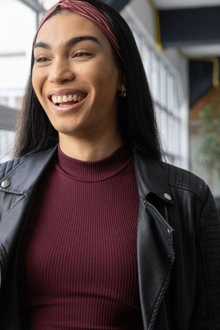 Smiling young woman wearing burgundy ribbed top and black leather jacket in modern atrium