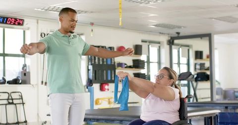 Therapist Guiding Woman in Wheelchair Using Resistance Band During Rehabilitation Session