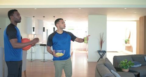 Friends watching game at home holding basketball, snacks and drinks in modern living room
