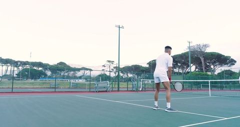 Male tennis player preparing to serve on outdoor court at dawn with mountain backdrop