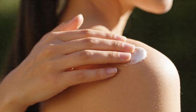 Sunlit shoulder skincare routine applying moisturizer to bare shoulder closeup, natural care