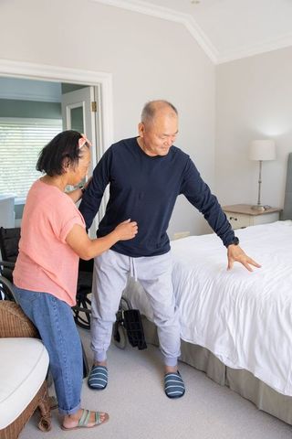 Asian senior man receiving bedside transfer help from partner for safe standing