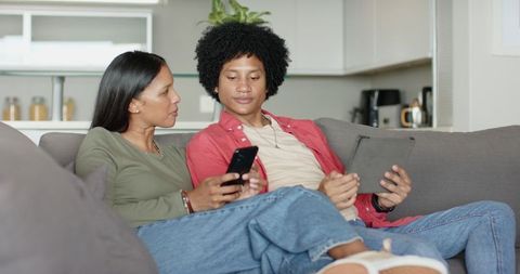 Diverse Couple on Sofa Sharing Content Using Smartphone and Tablet