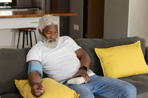 Senior african american man measuring blood pressure on couch with wrist cuff and monitor