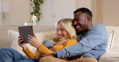 Happy Couple Relaxing on Sofa Watching Content on Tablet Together