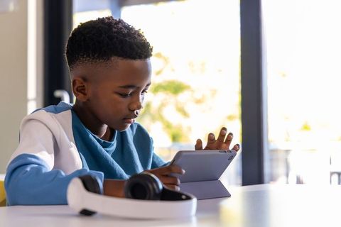 African american boy using tablet and headphones while studying at home and focusing