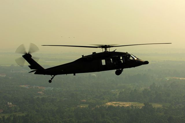 A military helicopter flying over a dense forest in dawn light creates a dramatic silhouette against the subtly lit sky. Useful for content related to aviation, military operations, or nature conservation. Ideal for blogs, articles, or advertising focused on aviation technology, military gear, or scenic landscapes.