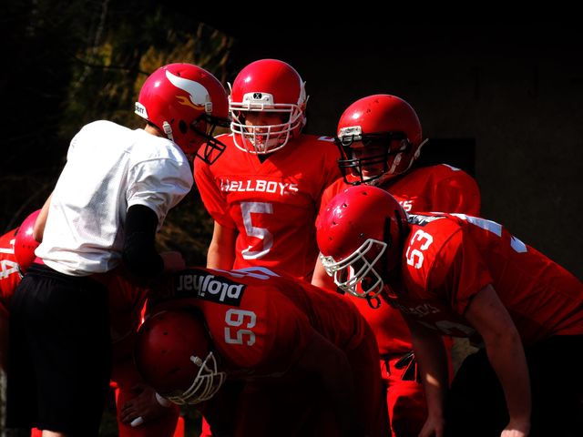 Football players in red uniforms and helmets gather in a huddle, discussing strategy during a game. Perfect for use in sports articles, athletics blogs, teamwork pieces, and competitive sports promotions.