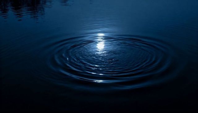 Moonlit water rippling creating concentric rings reflecting soft light on dark pond