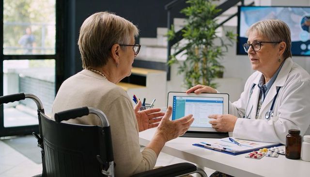 Doctor showing tablet to senior patient in wheelchair during medical consultation