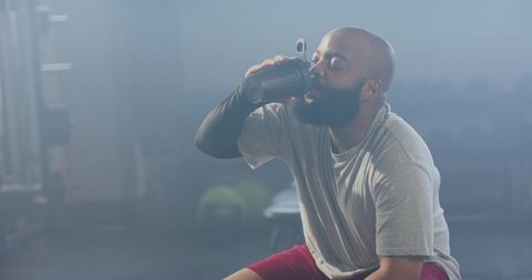 African american athlete drinking protein shake while resting on gym bench after workout