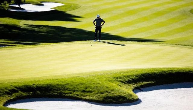 Golfer lining up long putt on sunlit championship golf course green