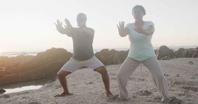 Senior couple is practicing Tai Chi on beach during sunrise. Both are focusing on their movements, embodying the spirit of exercise. This is ideal for promoting wellness, fitness routines for seniors, and mental health awareness, especially within tranquil outdoor environments.