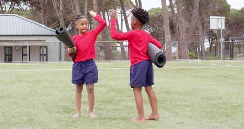 Youthful boys giving high five outdoors with exercise mats