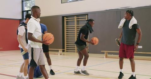 Five male players dribbling basketballs in school gym practicing teamwork and conditioning