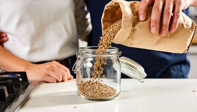Pouring lentils from brown paper bag into glass jar for eco-friendly pantry storage